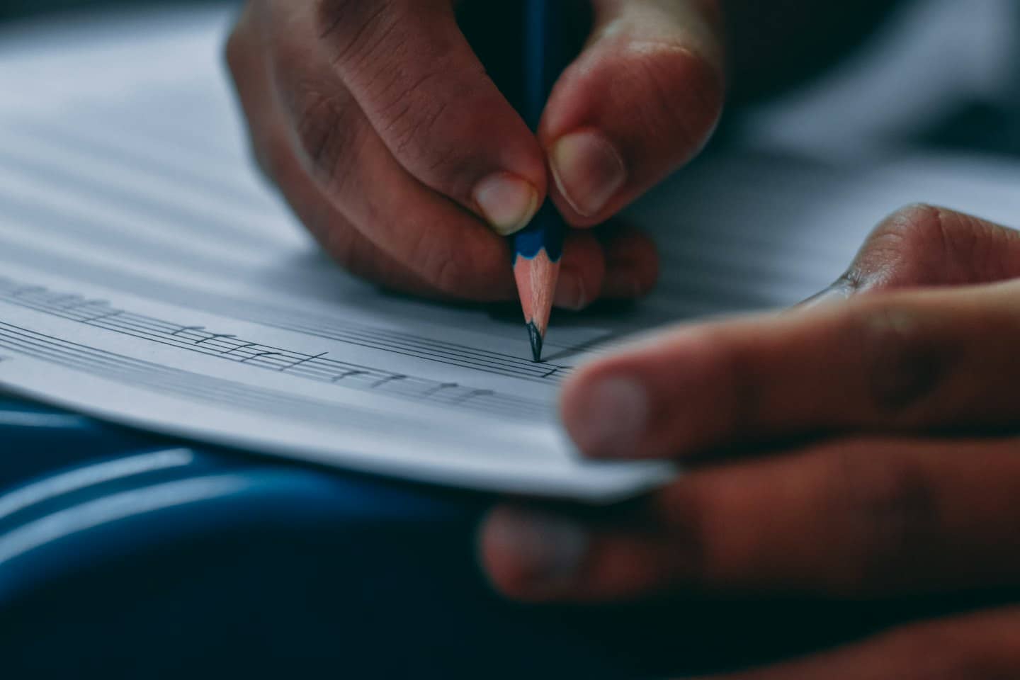 Hands holding a colorful pencil writing music on staff paper.