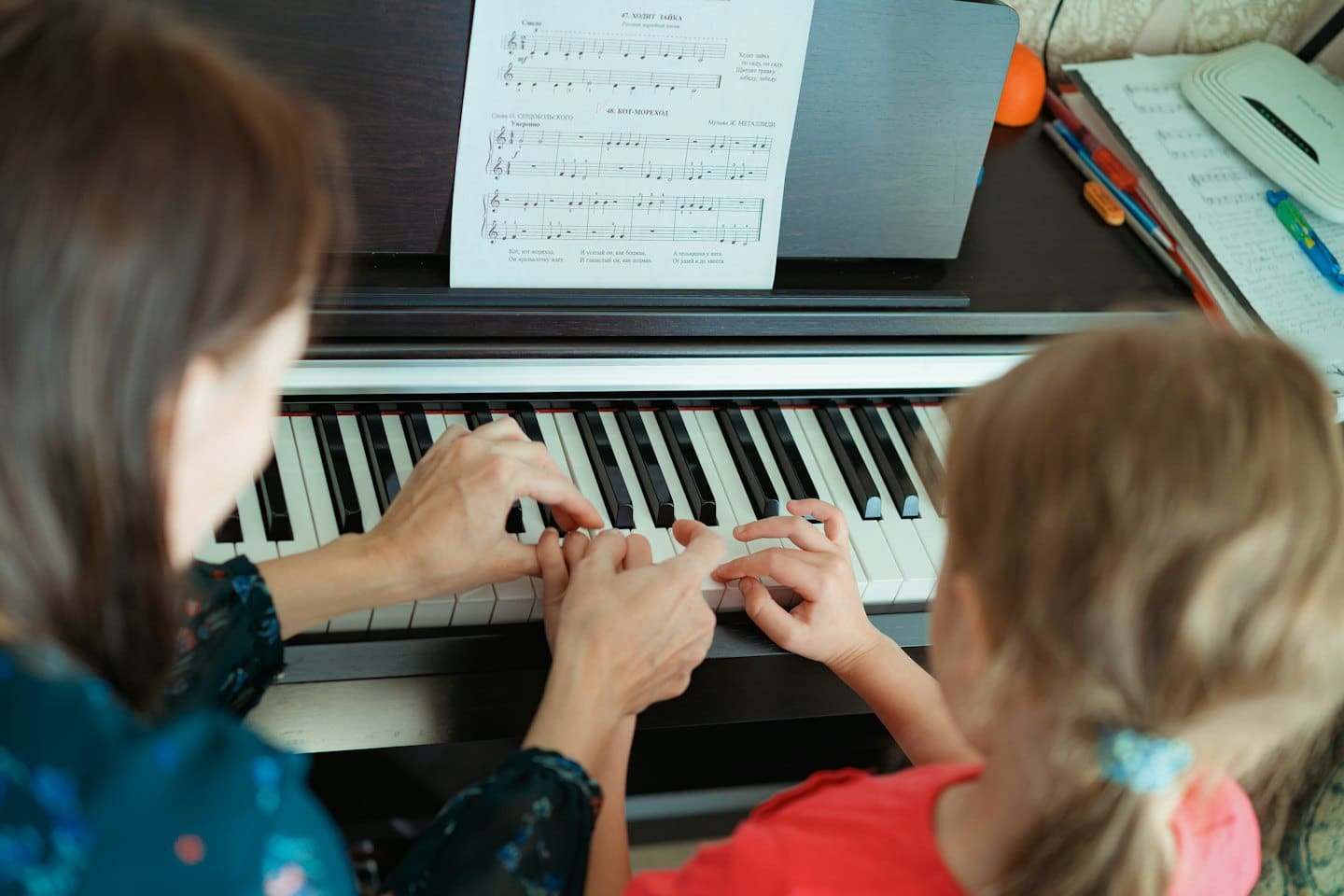 An adult teaches a young child to play the piano.