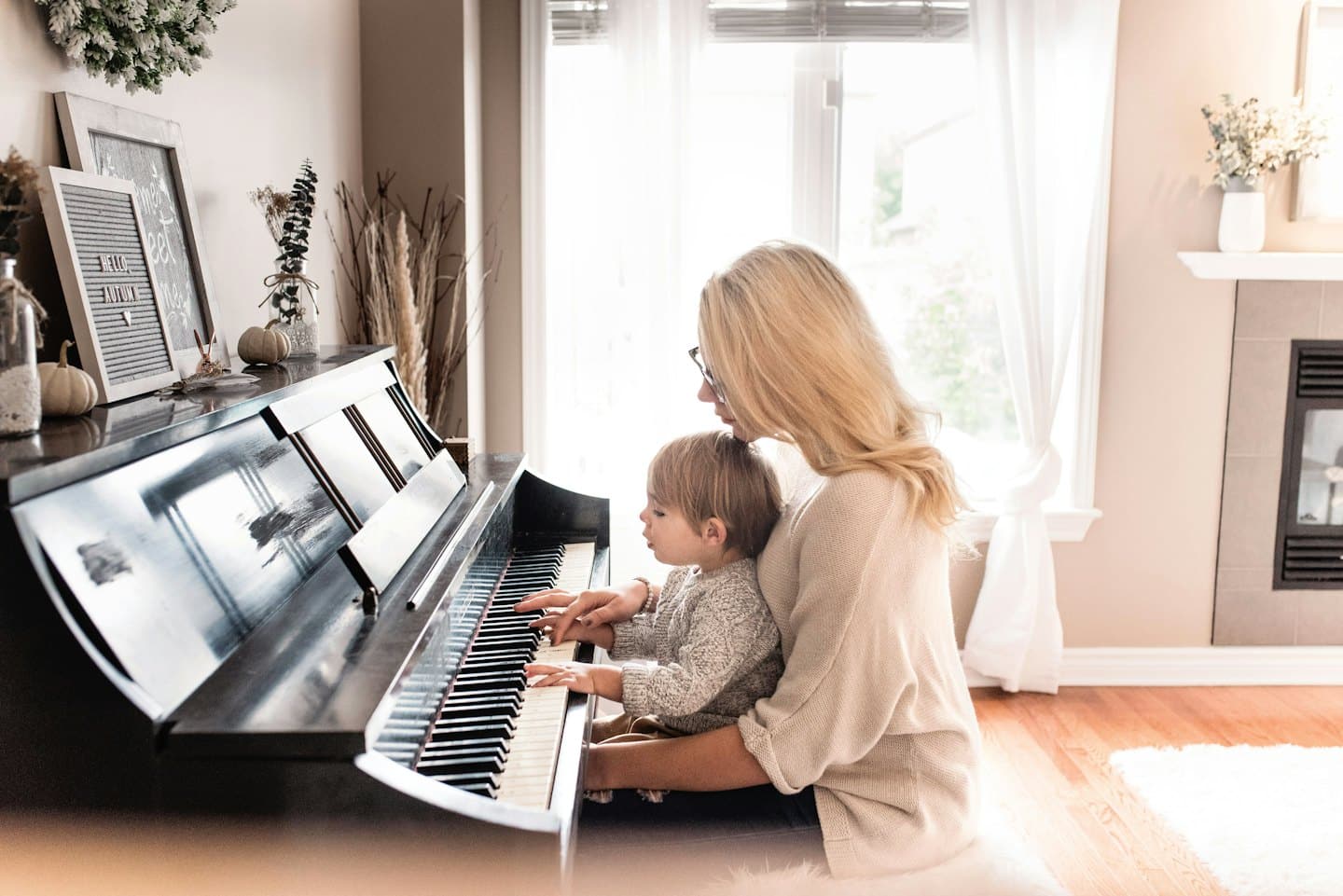 Woman teaches child to play piano with pumpkins on top.